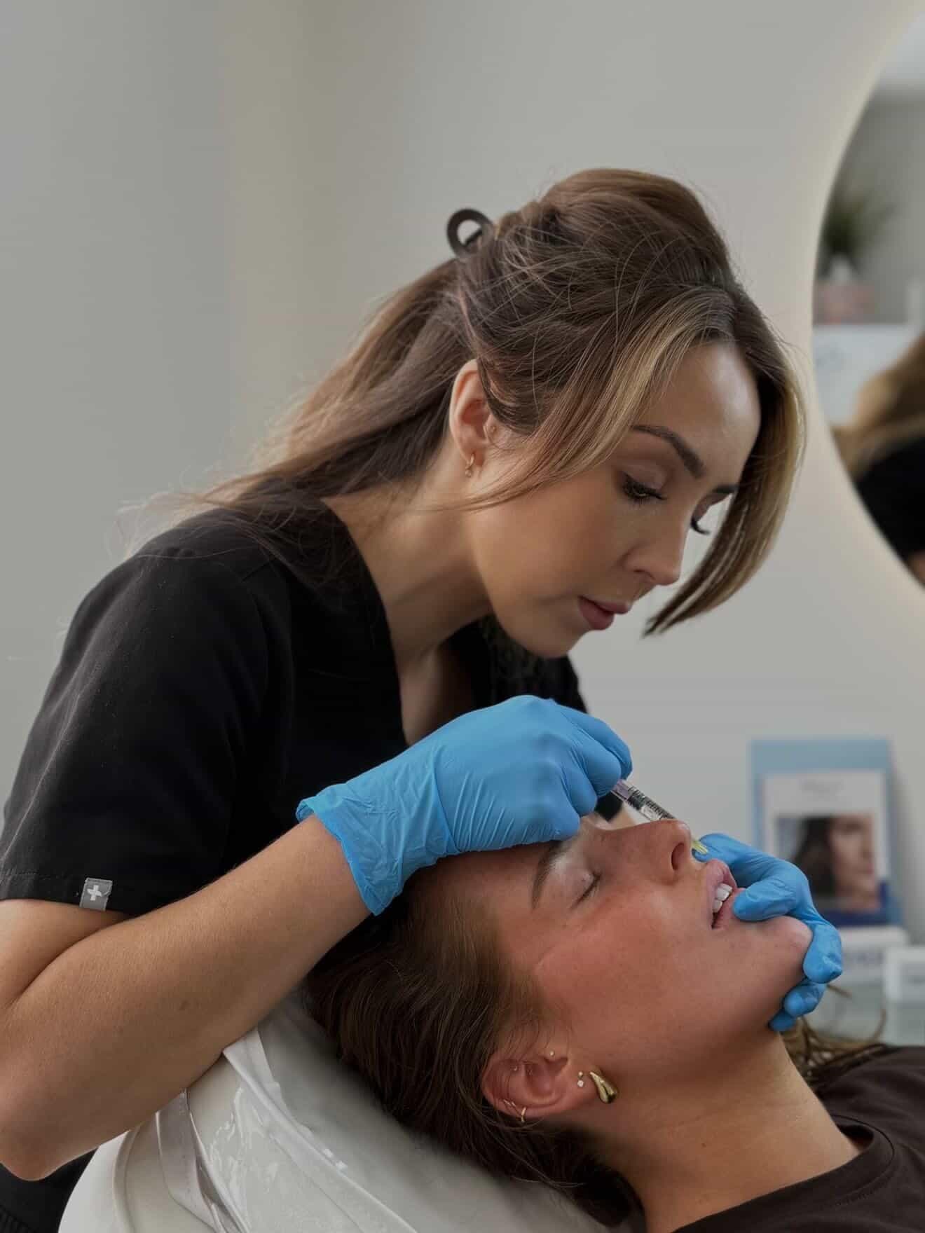 Amy, in black scrubs and blue gloves, treating a client's lips