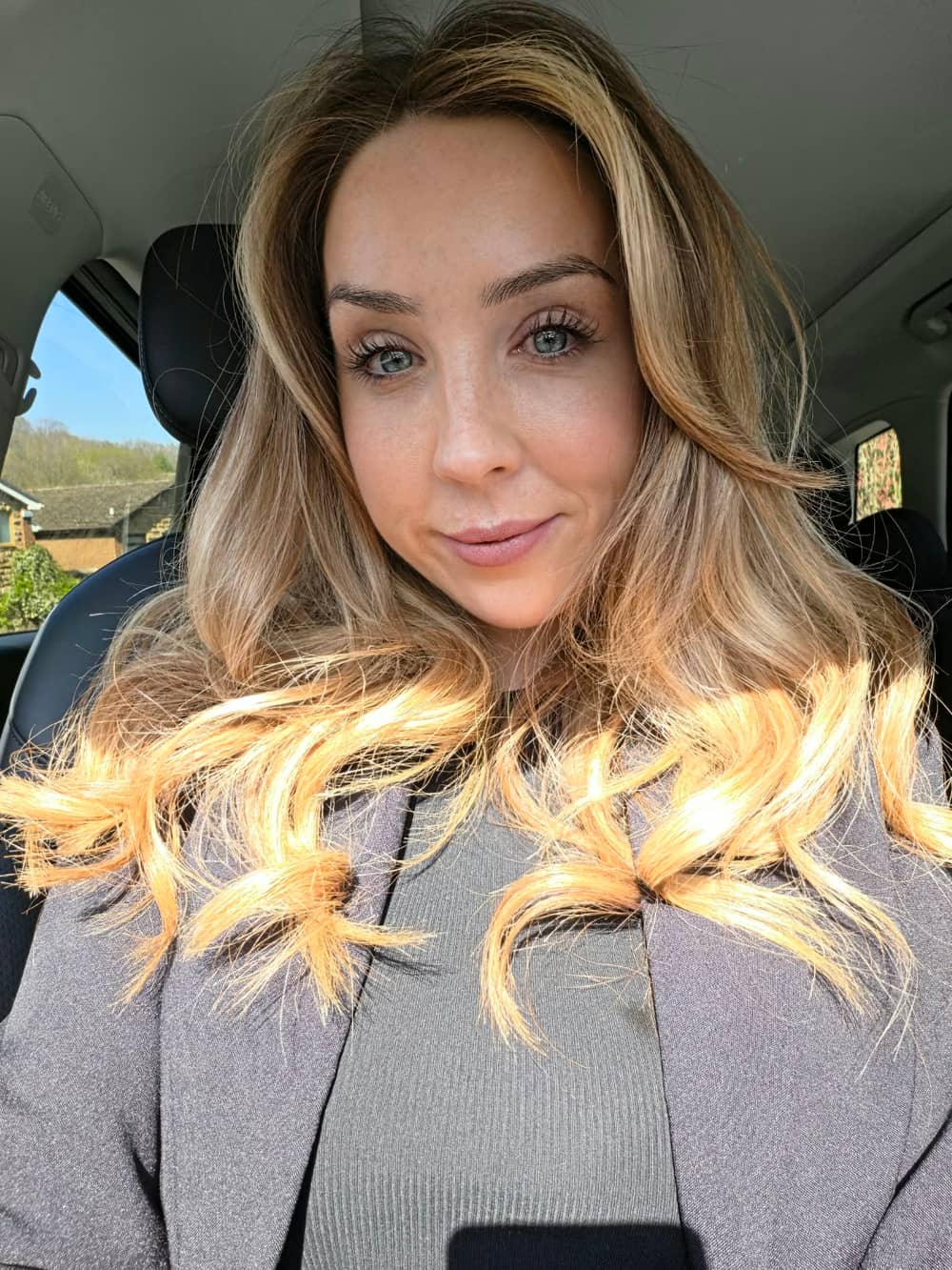 Amy Lisle with a soft smile, long wavy blonde hair over a grey blazer